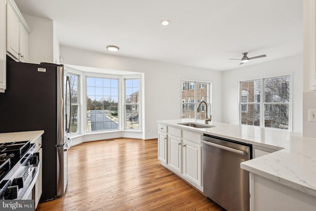 kitchen featuring light stone counters, light wood-style floors, white cabinets, stainless steel appliances, and a sink