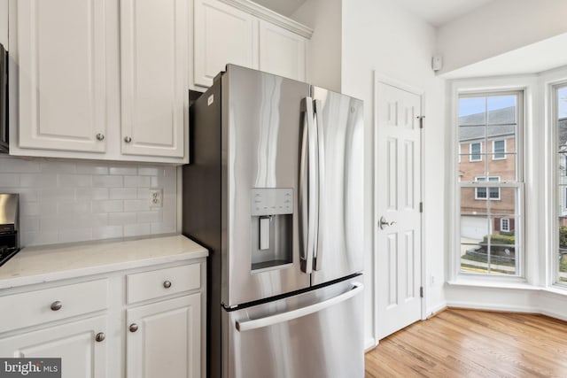 kitchen featuring light wood-type flooring, stainless steel fridge, tasteful backsplash, and white cabinets