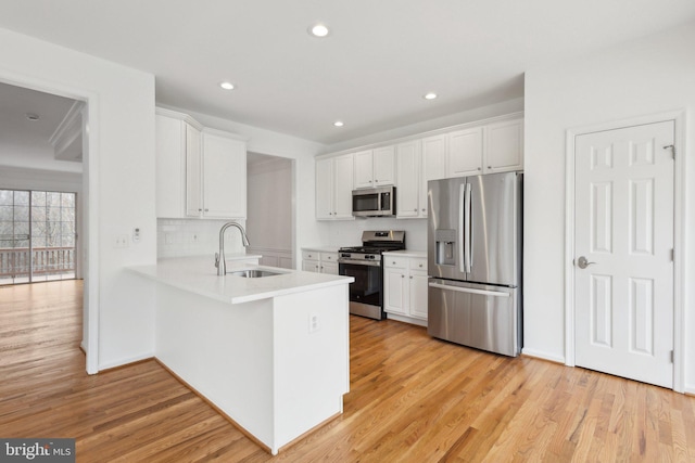 kitchen with light wood finished floors, a sink, light countertops, white cabinets, and appliances with stainless steel finishes