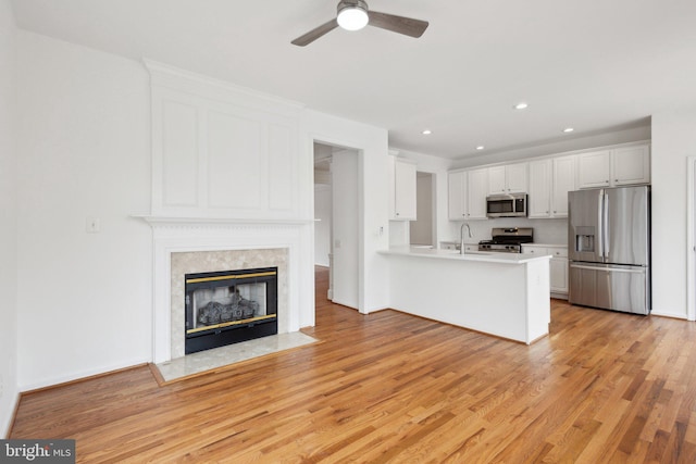 kitchen featuring a sink, white cabinetry, stainless steel appliances, a peninsula, and light wood finished floors