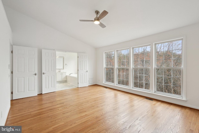 interior space featuring a ceiling fan, visible vents, lofted ceiling, ensuite bathroom, and light wood-type flooring