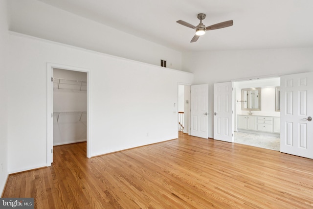 unfurnished bedroom featuring lofted ceiling, a spacious closet, light wood-style floors, a closet, and ensuite bathroom