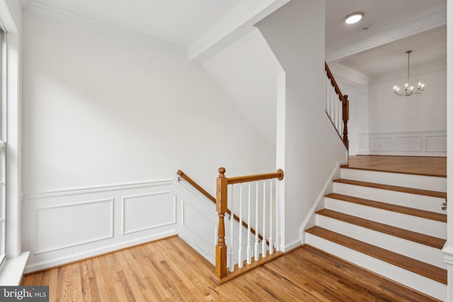 staircase featuring a chandelier, ornamental molding, wainscoting, wood finished floors, and a decorative wall