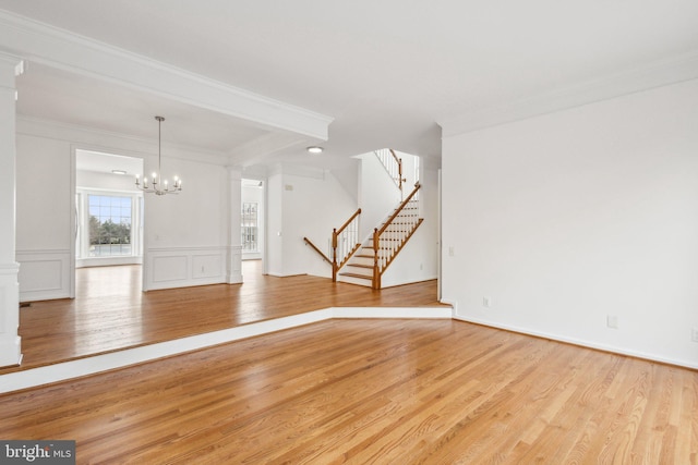 unfurnished living room featuring a decorative wall, stairway, ornamental molding, light wood-style flooring, and a notable chandelier