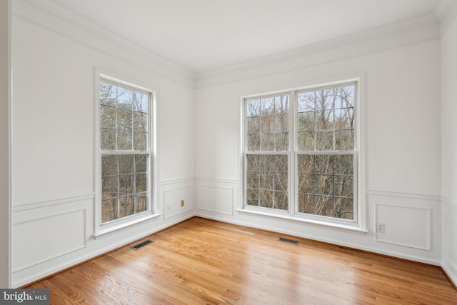 unfurnished room featuring wainscoting, visible vents, light wood-style flooring, and crown molding