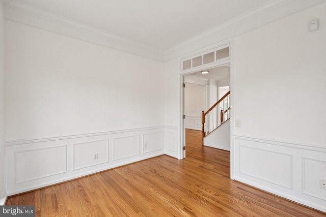 empty room featuring light wood-type flooring, ornamental molding, and wainscoting