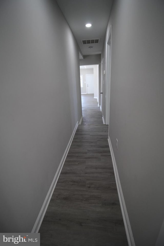 hallway with dark wood finished floors, visible vents, and baseboards