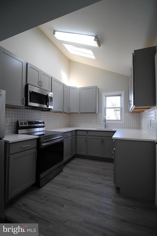 kitchen featuring lofted ceiling with skylight, gray cabinets, stainless steel appliances, light countertops, and a sink