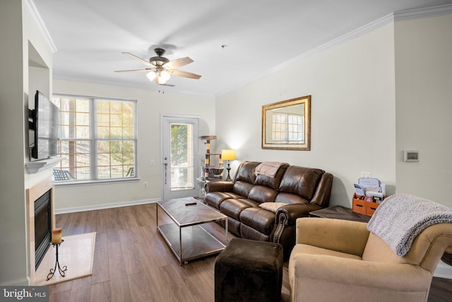 living area with baseboards, a glass covered fireplace, crown molding, and wood finished floors