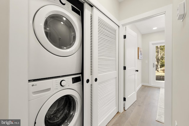 clothes washing area with laundry area, light wood finished floors, stacked washer and clothes dryer, and baseboards