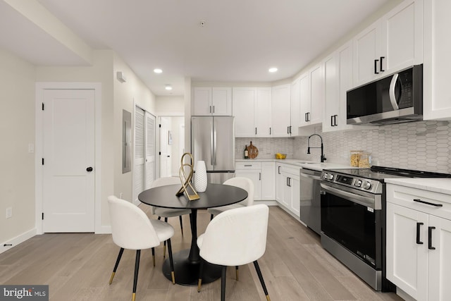 kitchen featuring light countertops, decorative backsplash, appliances with stainless steel finishes, white cabinets, and a sink