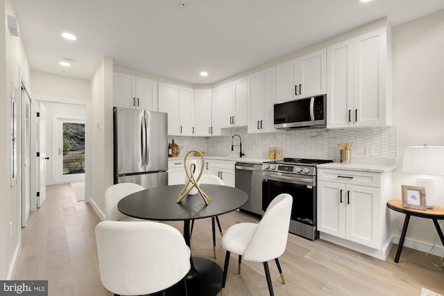 kitchen featuring appliances with stainless steel finishes, white cabinets, light wood-style flooring, and decorative backsplash