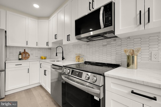 kitchen featuring white cabinetry, appliances with stainless steel finishes, decorative backsplash, and a sink