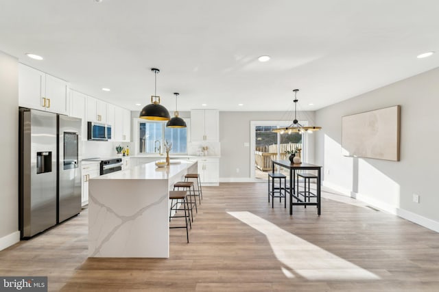 kitchen with light wood-style floors, a kitchen island with sink, appliances with stainless steel finishes, and a kitchen breakfast bar