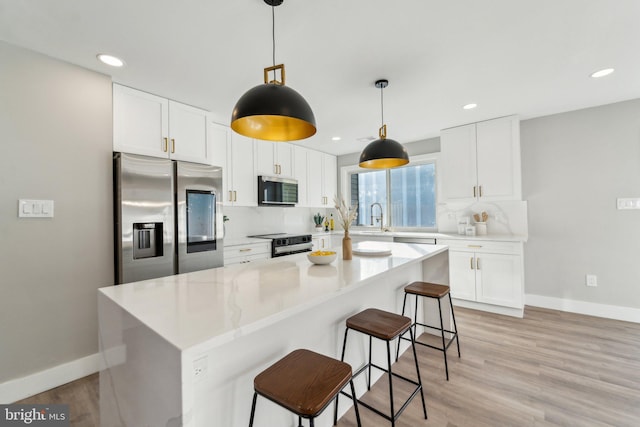 kitchen featuring light wood finished floors, decorative backsplash, a breakfast bar area, stainless steel appliances, and a sink