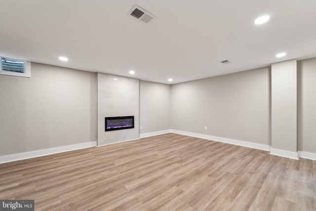 finished below grade area with light wood-type flooring, visible vents, a fireplace, and recessed lighting