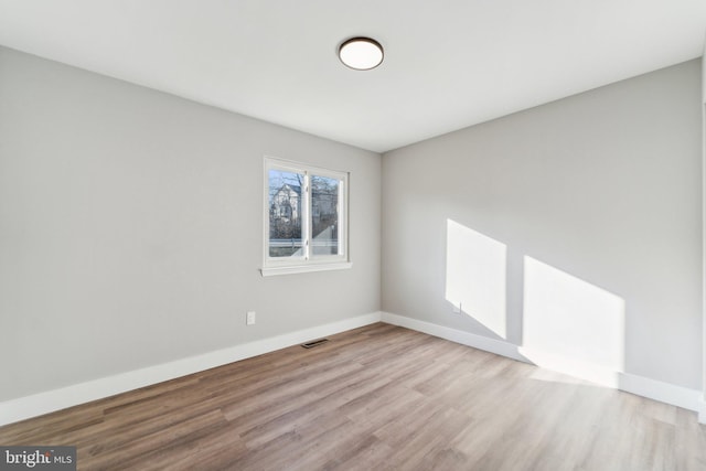 spare room with wood finished floors, visible vents, and baseboards