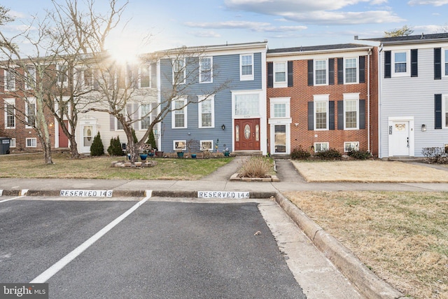 view of property with uncovered parking, brick siding, a front yard, and a residential view