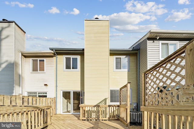 rear view of house with a deck, fence, a chimney, and central AC unit