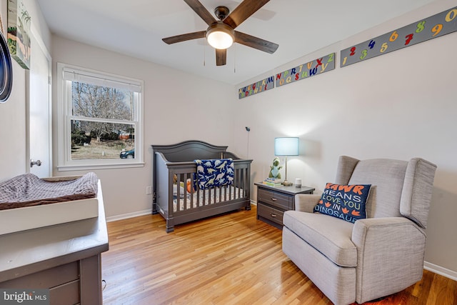 bedroom with light wood-style floors, a crib, baseboards, and a ceiling fan