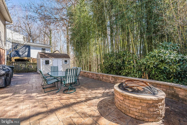 view of patio featuring a fire pit, an outbuilding, a grill, a storage unit, and fence