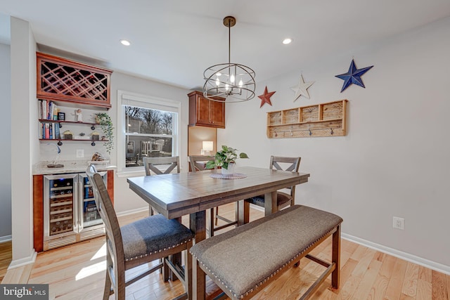 dining area with beverage cooler, bar, light wood-style flooring, and baseboards