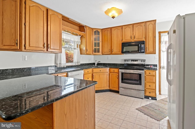 kitchen featuring glass insert cabinets, a sink, dark stone countertops, white appliances, and a peninsula