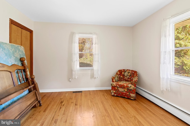 sitting room with light wood-type flooring, a baseboard radiator, visible vents, and baseboards