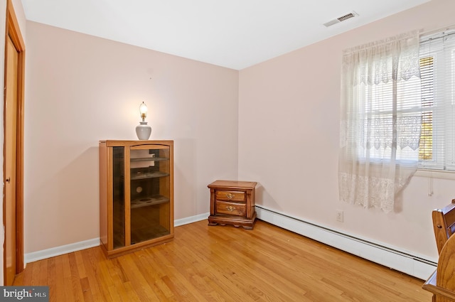 unfurnished room with baseboards, visible vents, baseboard heating, and wood finished floors