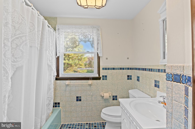 full bathroom featuring tile walls, toilet, wainscoting, vanity, and a bath