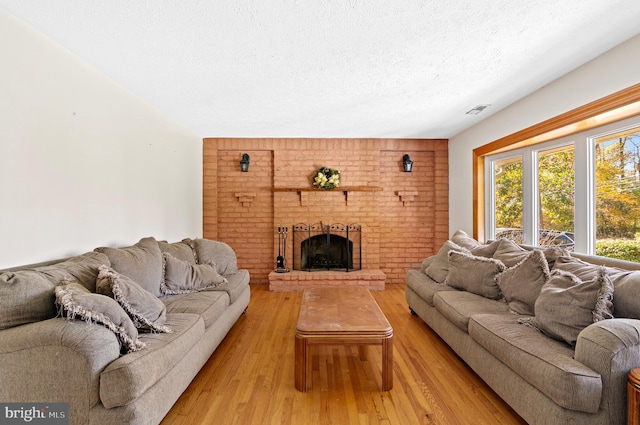 living area featuring a textured ceiling, a brick fireplace, wood finished floors, and visible vents