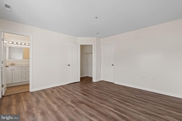 unfurnished bedroom with visible vents, a sink, ensuite bath, wood finished floors, and baseboards