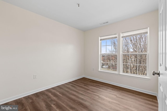 empty room featuring baseboards, visible vents, and dark wood-type flooring