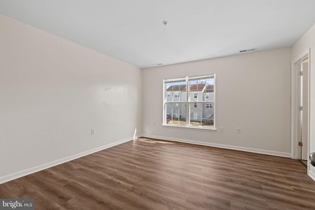 empty room featuring dark wood finished floors, visible vents, and baseboards