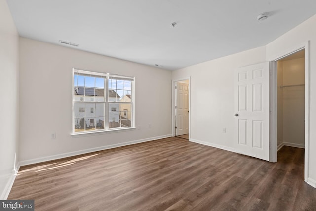 unfurnished bedroom featuring baseboards, visible vents, a walk in closet, and wood finished floors