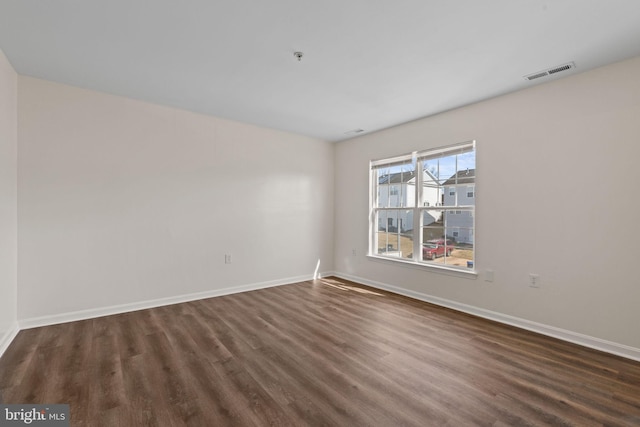 empty room with dark wood-style floors, visible vents, and baseboards