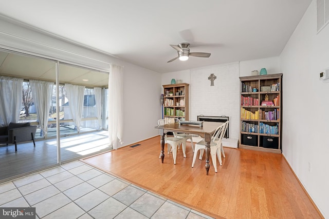 dining area featuring a ceiling fan, a brick fireplace, light wood-style floors, and visible vents