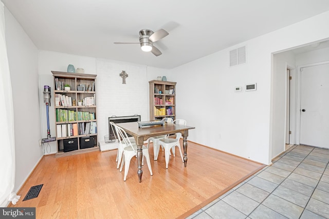 dining space featuring visible vents, light wood-style floors, a brick fireplace, and ceiling fan