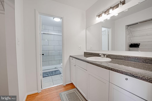 bathroom with toilet, wood finished floors, a shower stall, baseboards, and vanity