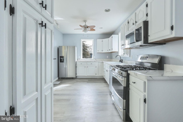 kitchen with appliances with stainless steel finishes, white cabinets, light countertops, and a sink