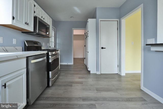 kitchen with baseboards, appliances with stainless steel finishes, light countertops, light wood-style floors, and white cabinetry