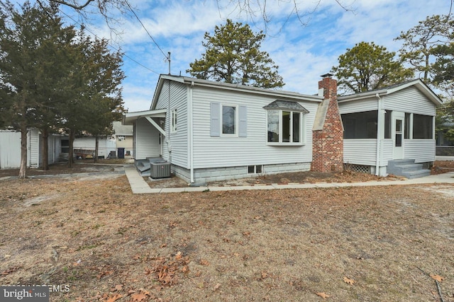 view of front of property with entry steps, central AC unit, a chimney, and a sunroom