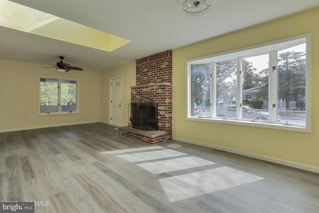 unfurnished living room with ceiling fan, a fireplace, light wood-style flooring, and baseboards