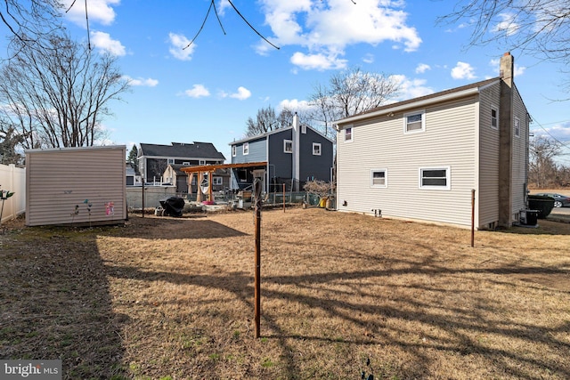 rear view of property with an outbuilding, a yard, a chimney, central AC unit, and fence