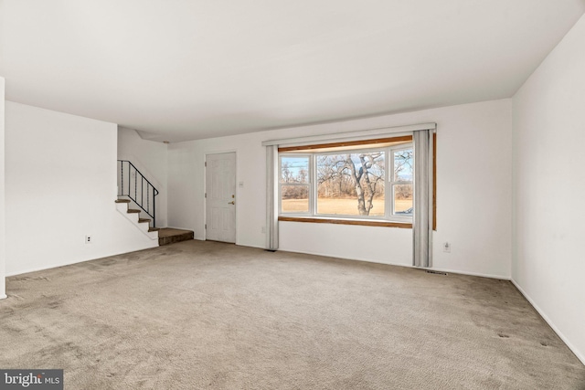 unfurnished living room featuring stairway and carpet flooring