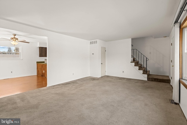 unfurnished living room with carpet, visible vents, ceiling fan, and stairs