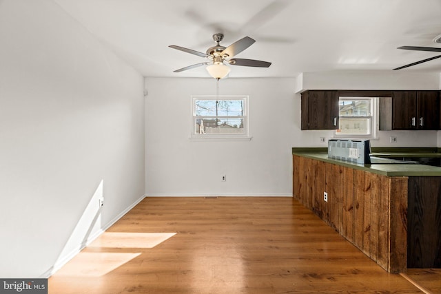 kitchen with dark countertops, light wood-type flooring, a ceiling fan, and baseboards