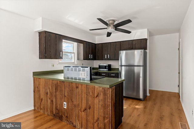 kitchen with light wood-style flooring, appliances with stainless steel finishes, ceiling fan, dark brown cabinetry, and a peninsula