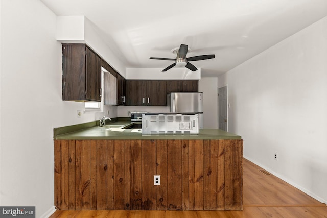 kitchen featuring light wood-style flooring, dark brown cabinetry, a peninsula, a sink, and freestanding refrigerator