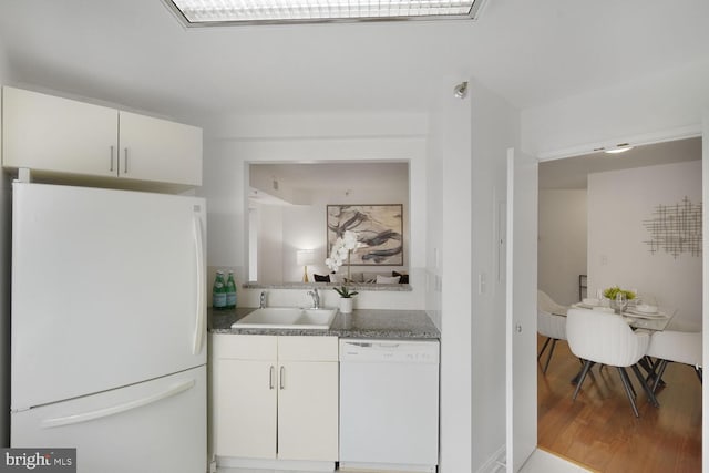 kitchen with white appliances, dark countertops, a sink, and white cabinets